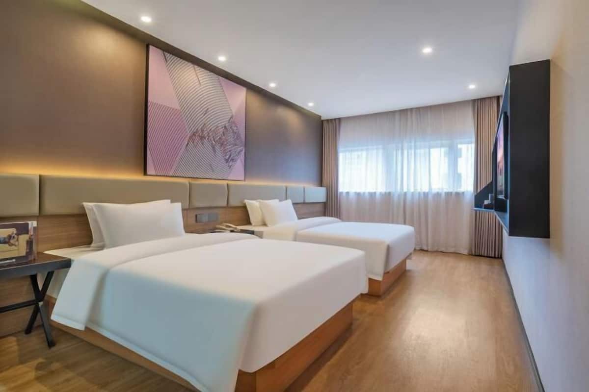 Une chambre d’hôtel avec deux lits, une grande peinture abstraite au mur, un téléviseur à écran plat fixé au mur et une fenêtre avec des rideaux.