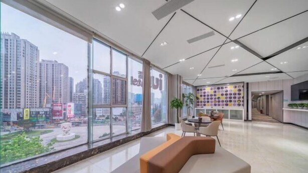 Een moderne hotellobby met een groot raam dat uitzicht biedt op de stad, een zithoek met een bank en stoelen, en een muur met een kleurrijk rond patroon.