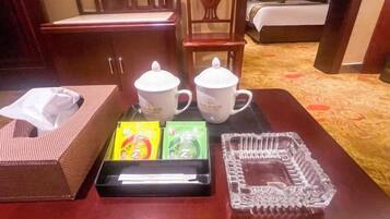 A hotel room with a wooden table, two white mugs, a tissue box, and a tray with items.