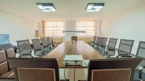 Una sala de conferencias con una larga mesa, sillas, un proyector y ventanas con cortinas.
