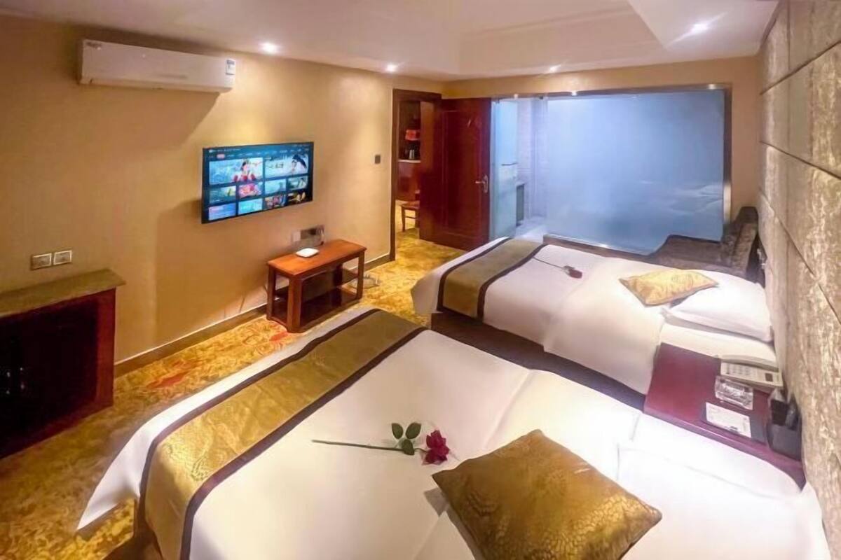 A hotel room with two beds, a TV, a small table, and an air conditioning unit.