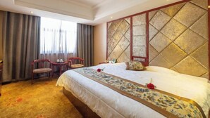 A hotel room with a large bed, a headboard with a geometric pattern, a small desk with a chair, and a window with curtains. - Jintaolai Hotel (Ejin Banner)