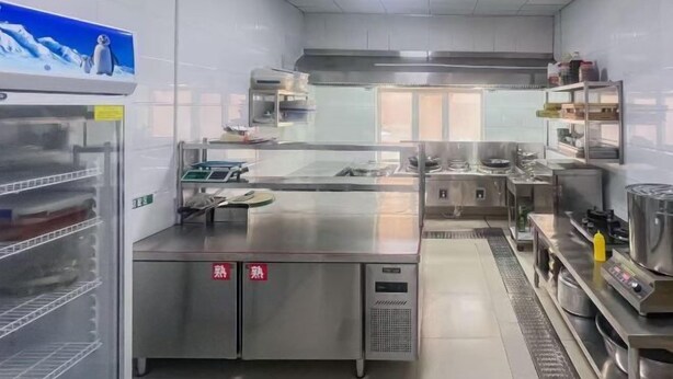 Una cocina industrial con electrodomésticos de acero inoxidable, un refrigerador grande y un mostrador expositor.