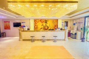 Zona de recepción de un hotel con bar, una lámpara de araña grande y un mostrador de recepción.