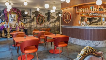 Uma área de bar com várias mesas e cadeiras, um balcão com um bartender e uma parede com quadros e um mural.