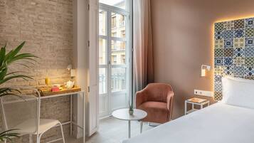 Habitación de hotel con pared de ladrillo, un ventanal grande, cama, una silla, una mesita con planta y decoración en la pared.