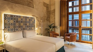A hotel room with a large bed, a decorative tiled headboard, a large window with a view, and a small table with a lamp. - Axel Hotel Valencia – Adults Only (Valencia)
