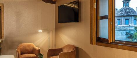 Una habitación con dos sillones marrones, una mesita blanca, un televisor de pantalla plana montado en la pared y un ventanal con vistas a un edificio con cúpula.