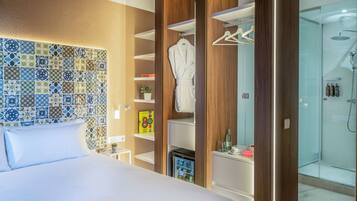 Habitación de hotel con cama, minibar, zona de ducha y armario con bata.