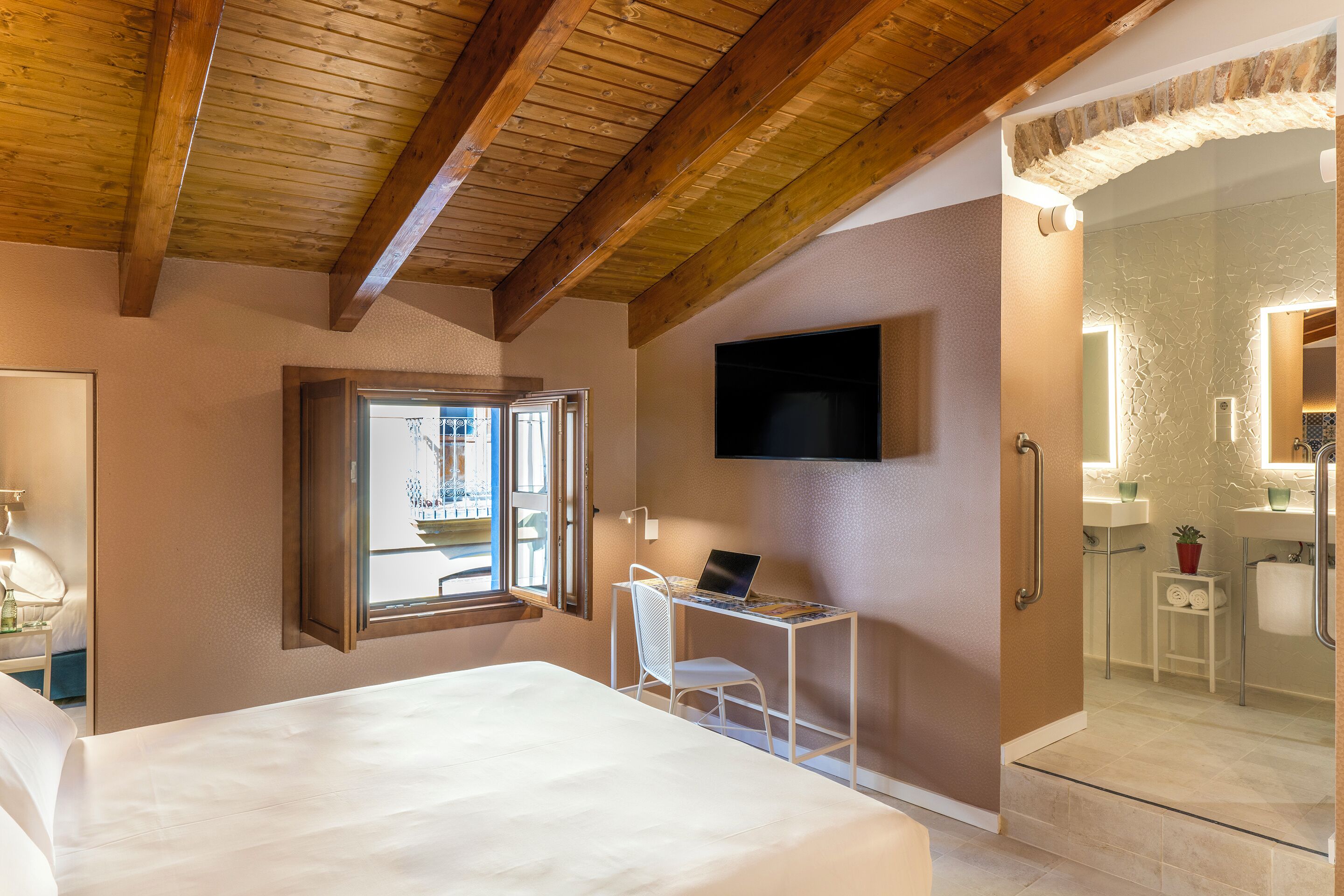 Un dormitorio con cama, escritorio con computadora portátil, televisor y baño con cabina de ducha de vidrio.