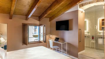 Un dormitorio con cama, escritorio con computadora portátil, televisor y baño con cabina de ducha de vidrio.