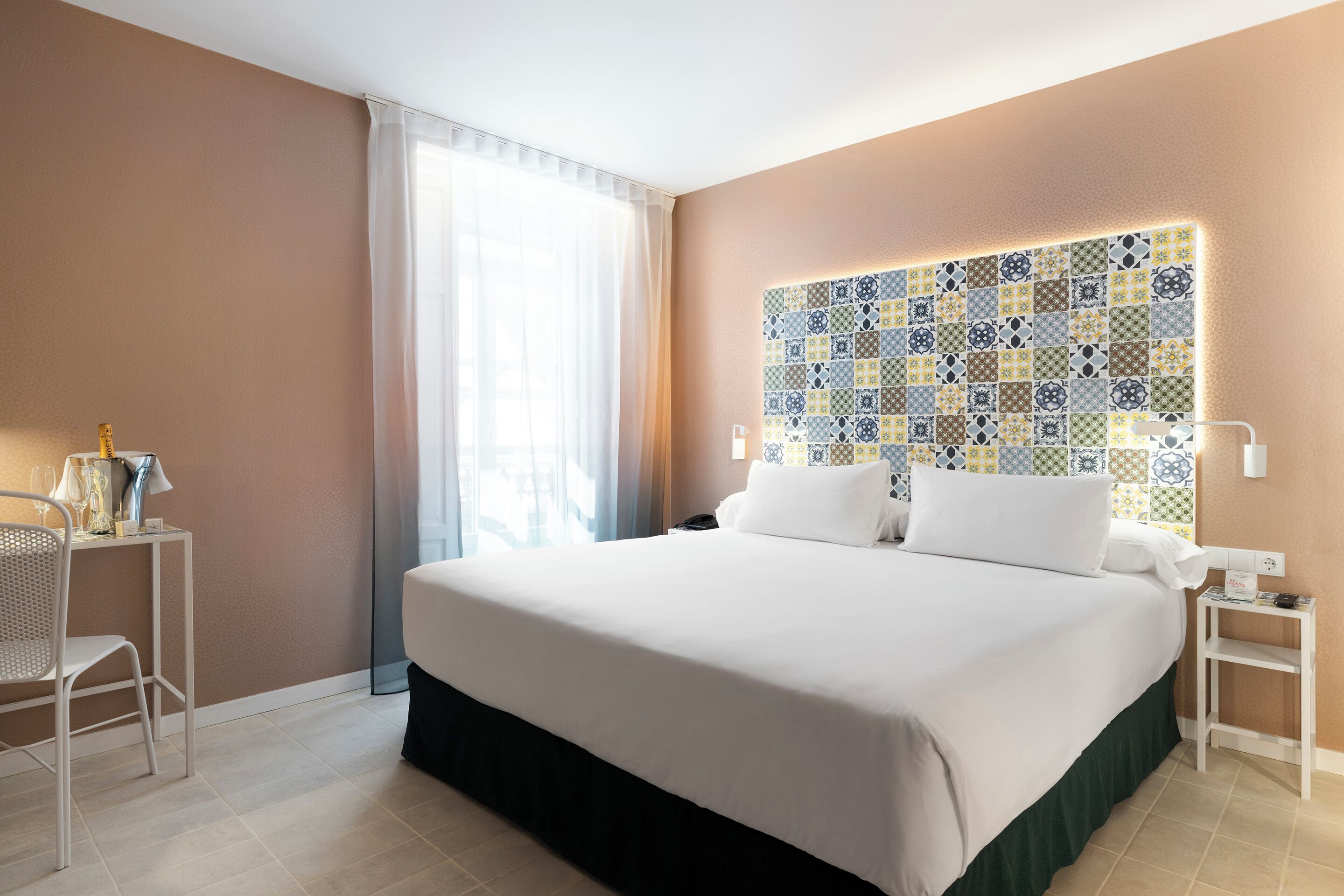 A hotel room with a large bed, a bedside table, a chair, and a window with curtains.