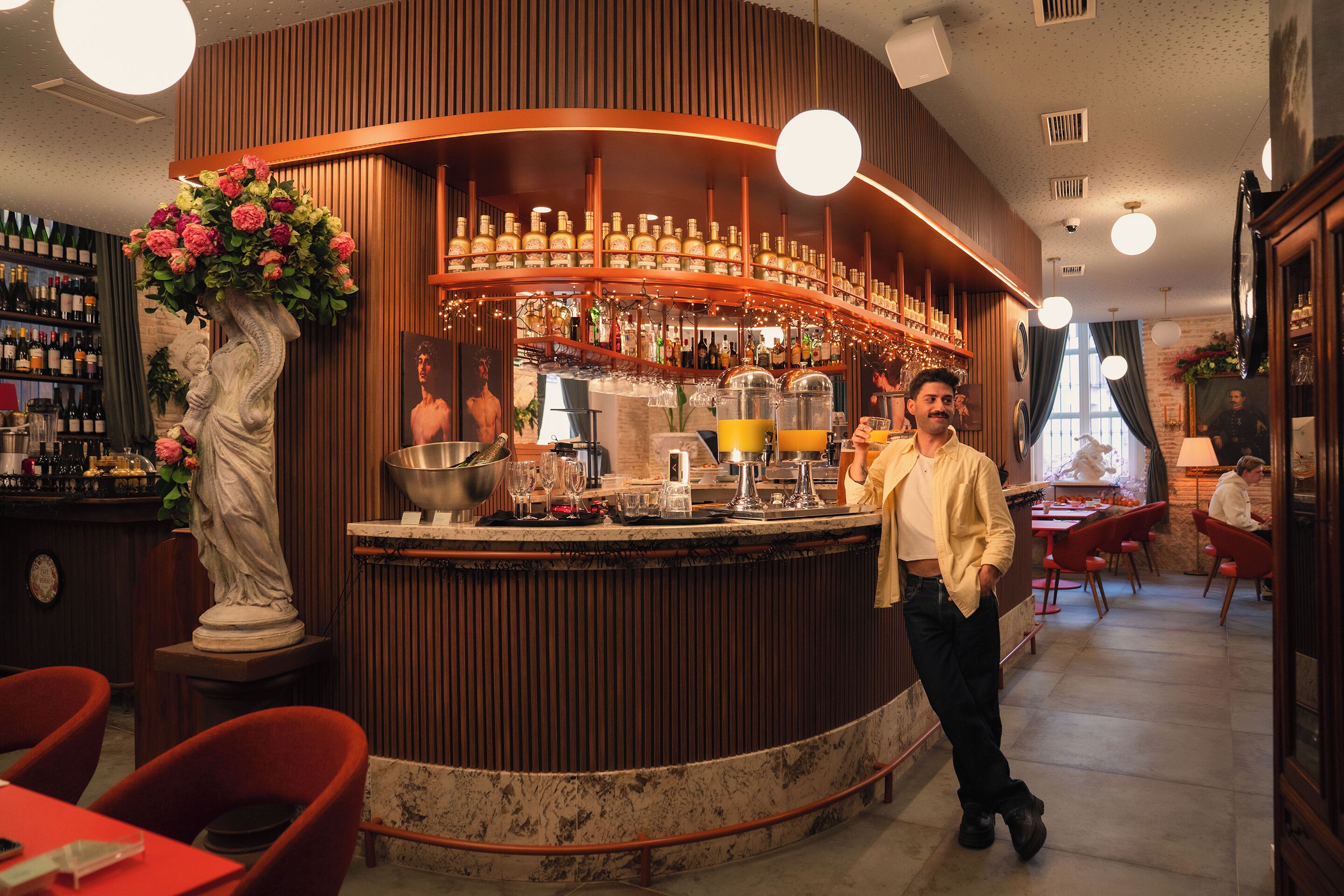 A bar area with a marble counter, bottles, glasses, and a statue.