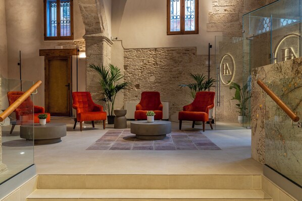 A lobby with red chairs, a wooden door, and a stone wall. - Axel Hotel Valencia – Adults Only (Valencia)