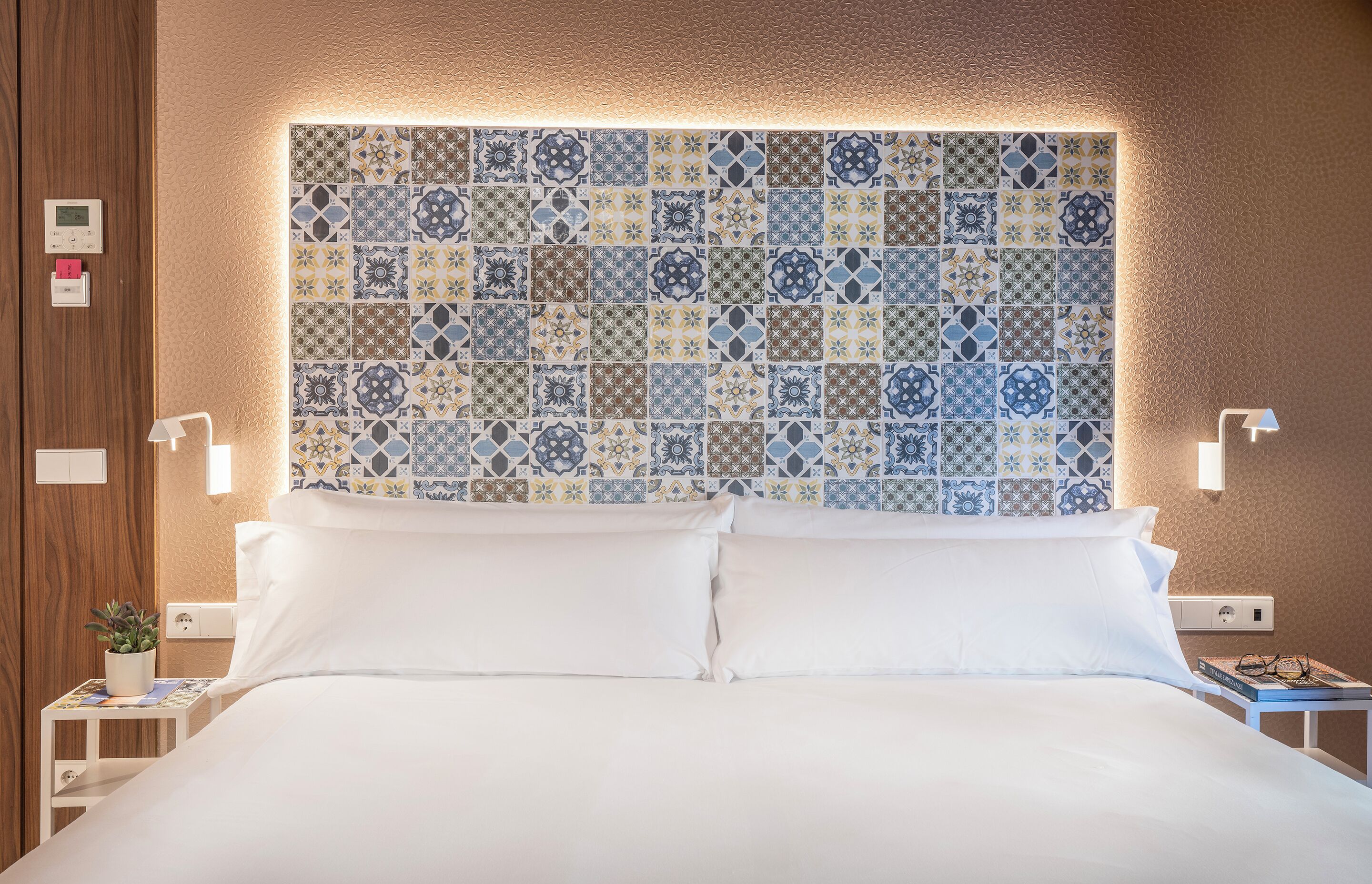 Una cama bien hecha con sábanas blancas, un cabecero de baldosas estampadas y lámparas de noche.