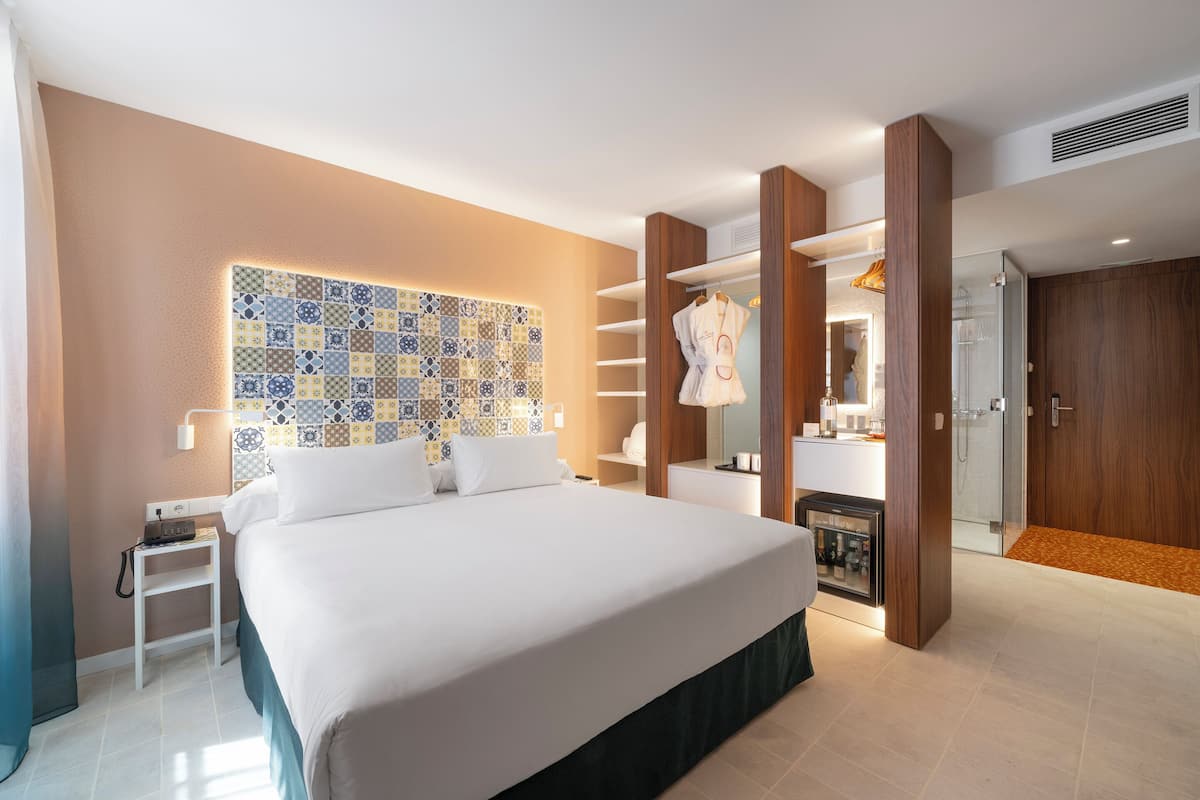 A modern hotel room with a large bed, a bedside table, a wardrobe, and a bathroom with a shower.