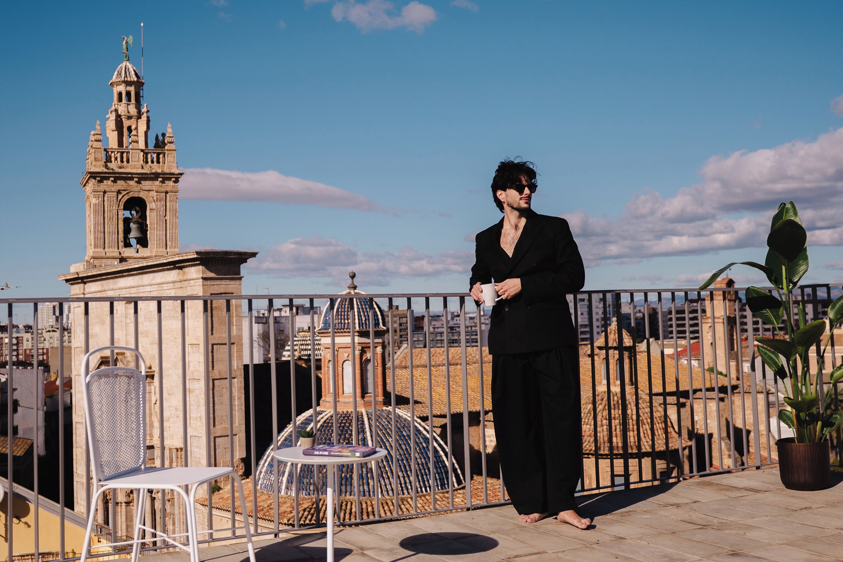 A person standing on a rooftop terrace with a view of a historic tower and cityscape.