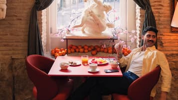 A dining area with a table set for two, a statue, and a view through a window.