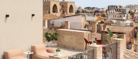 A rooftop terrace with a beige wall, a small table, a sofa, and potted plants.