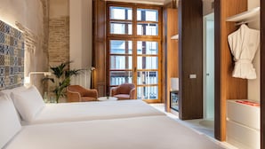 A hotel room with a large bed, two chairs, a potted plant, a wooden wardrobe, and a large window with a view of the outside. - Axel Hotel Valencia – Adults Only (Valencia)
