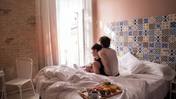 Una cama con una bandeja de desayuno, una silla blanca y una pared de ladrillo.