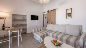Una sala moderna con un sofá a rayas, una mesa de comedor con sillas, un televisor montado en la pared y un estante pequeño con objetos decorativos.