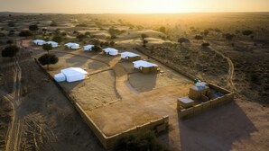 Une vue aérienne d’un village situé dans le désert, avec plusieurs constructions aux toits blancs, dont certaines sont surmontées de tentes, et quelques petits bâtiments aux toits plats.