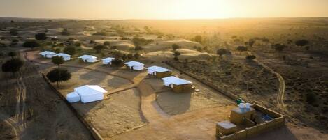 Vista aérea de un asentamiento en el desierto con varias estructuras de techos blancos, algunas con tiendas de campaña adosadas, y unos pocos edificios pequeños con techos planos.