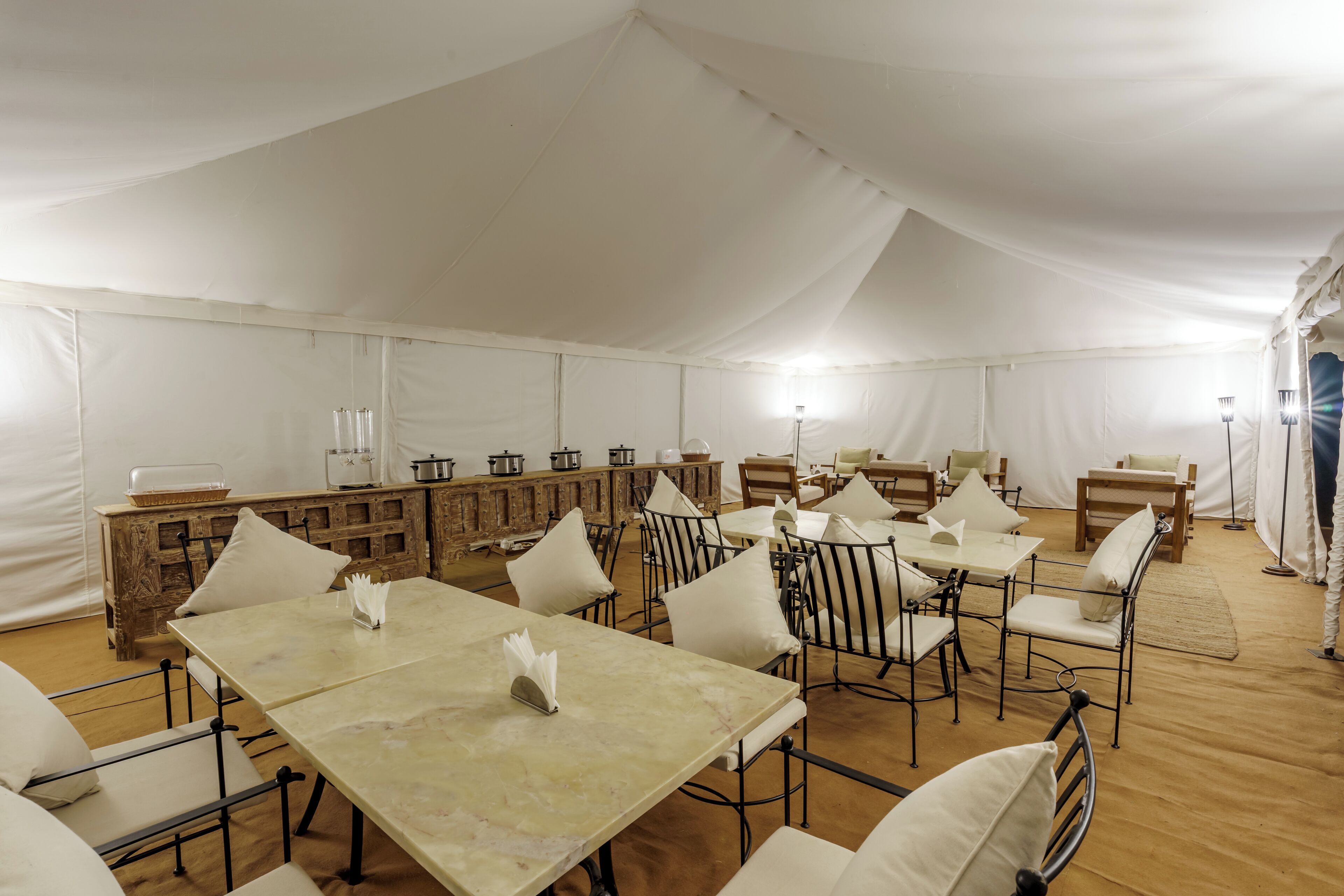 Un'area pranzo allestita con tende, tavoli e sedie, un buffet in legno e una grande tenda bianca.