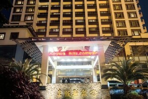 Entrada d'un hotel amb un senyal vermell prominent, façana de vidre i una zona d'aparcament amb cotxes.