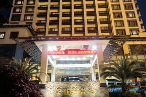 Entrada de hotel con un llamativo letrero rojo, fachada de vidrio y una zona de estacionamiento con vehículos.