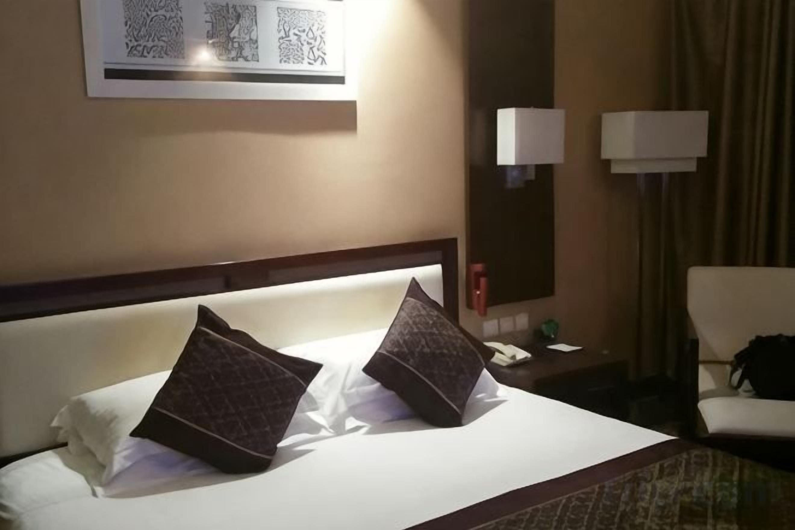Habitación de hotel con una cama, dos almohadas, una mesita de noche, una lámpara y una silla.