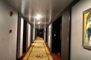 Un pasillo de hotel con piso alfombrado, puertas a ambos lados y un cuadro en la pared derecha.