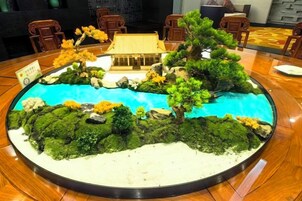 Una mesa redonda con un modelo a escala de un paisaje que incluye un edificio, árboles y una masa de agua.