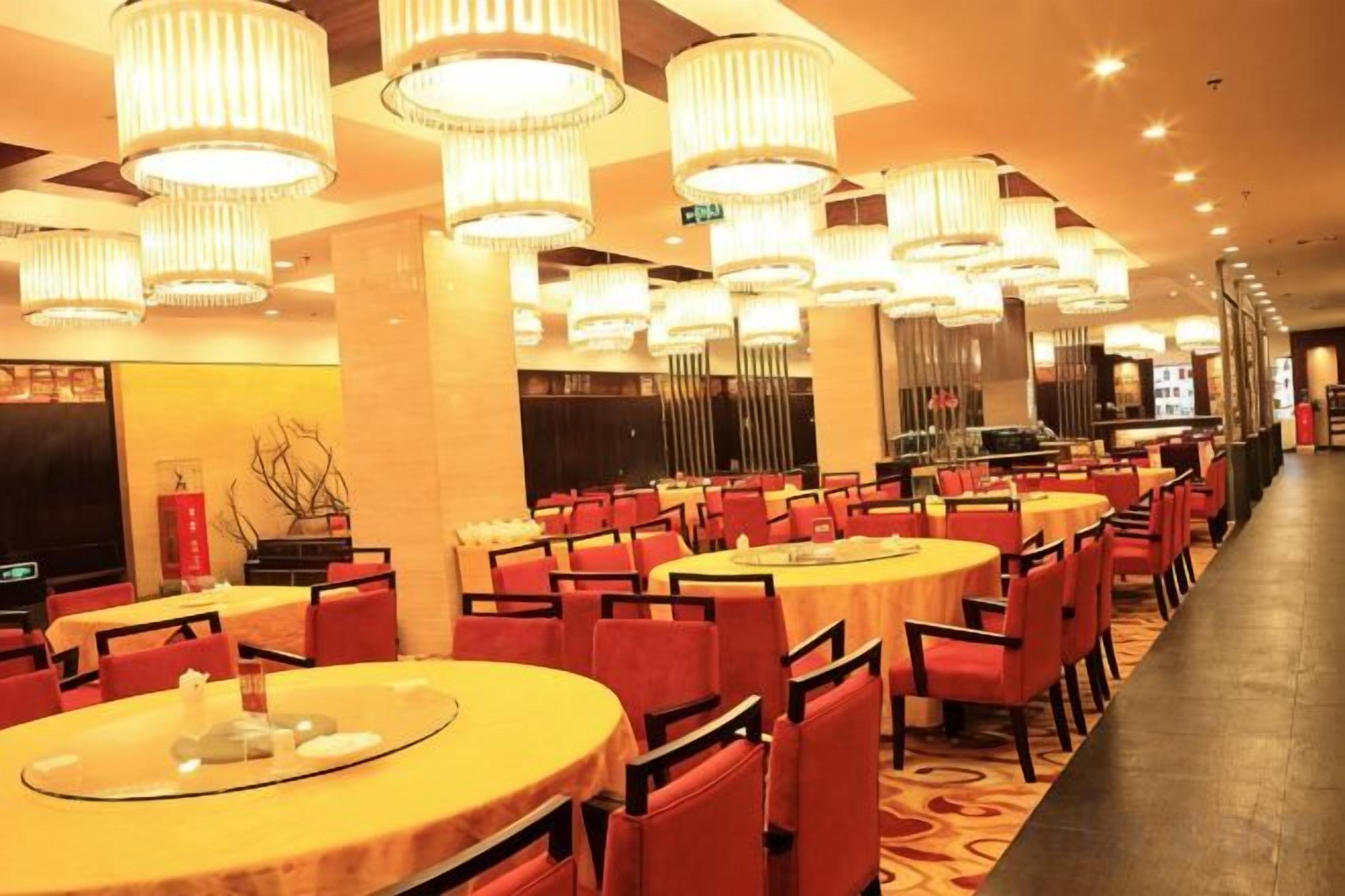 Un restaurant avec des tables rondes et des chaises rouges, de nombreux luminaires suspendus et un long comptoir.