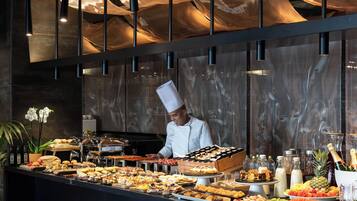 Montaje de bufé con diferentes alimentos y un chef preparándolos.