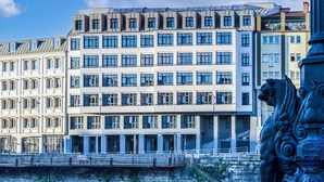 Un edificio moderno con múltiples ventanas y balcones, un muro de piedra y una estatua.