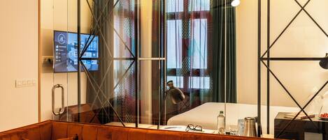 A modern hotel room with a glass partition, a television, a bed, a coffee machine, and a sofa.