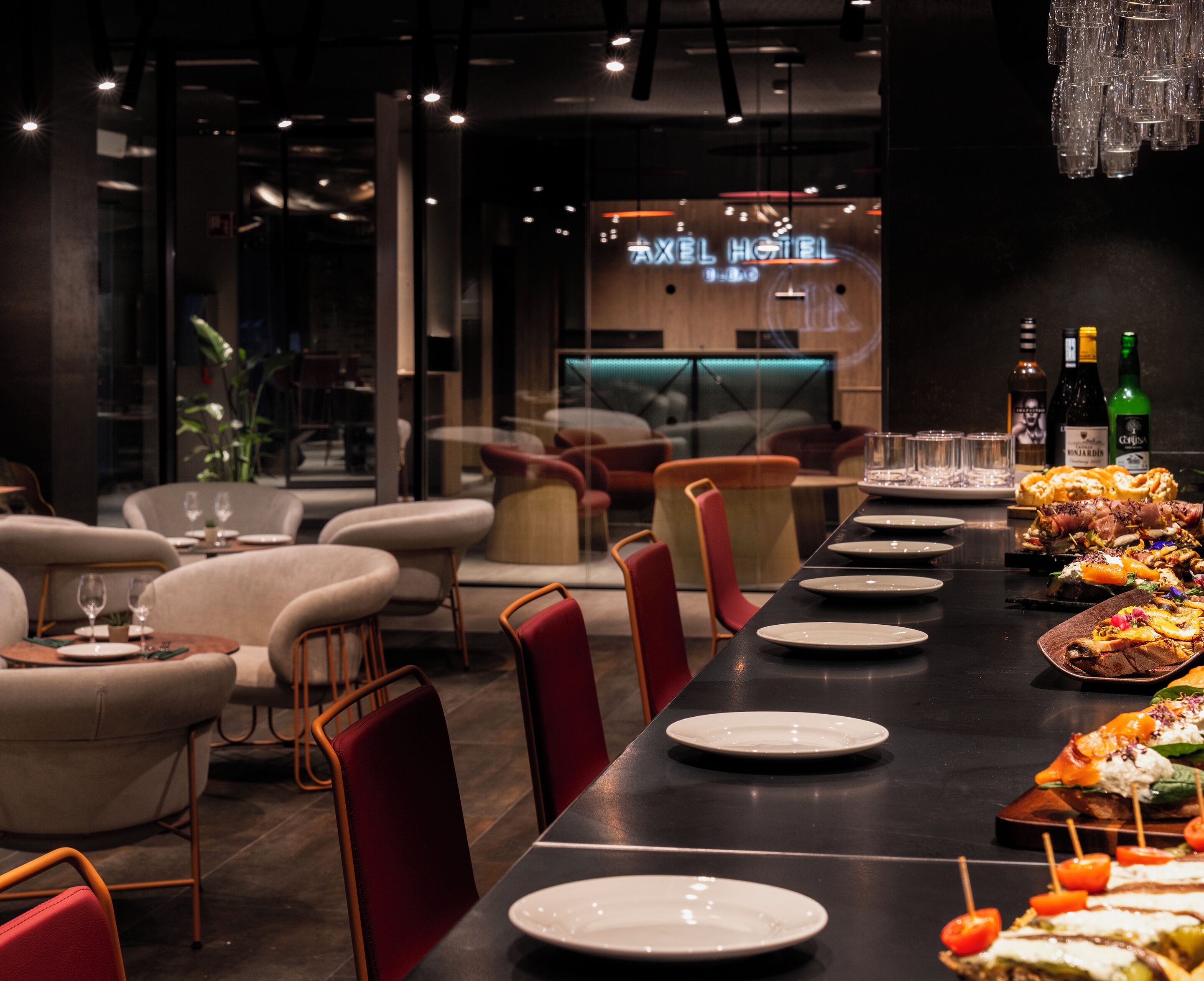 A restaurant with a long table set for dining, chairs, and a bar area in the background.