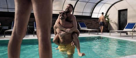 Una piscina con techo de vidrio, sillas de descanso y una puerta al fondo.