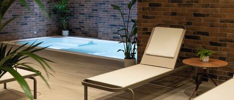 Een modern binnenzwembad met een bakstenen muur, lounge fauteuils en potplanten.