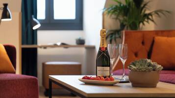 A bottle of Moët & Chandon champagne, two glasses, and a plate of strawberries on a wooden table in a living room with a sofa and a potted plant.