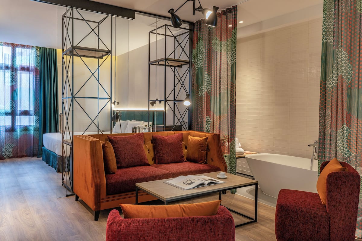 Une chambre d’hôtel moderne équipée d’un canapé, d’un fauteuil et d’une baignoire.