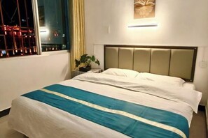 A neatly made bed with a striped bedspread, a bedside table with a plant, and a window with a view of city lights.