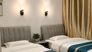 Habitación de hotel con dos camas, una mesita de noche con una planta y luces fijadas a la pared.
