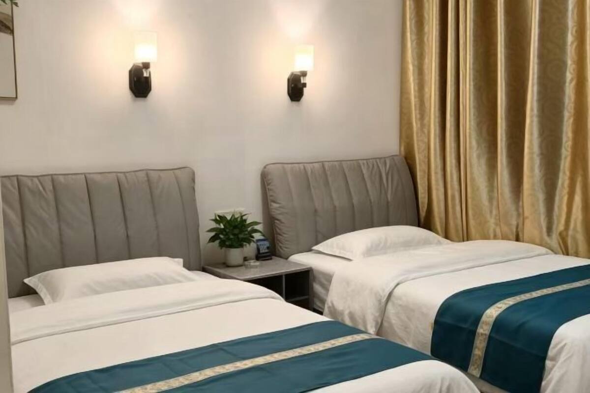 A hotel room with two beds, a nightstand with a plant, and wall-mounted lights.
