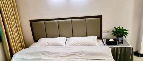 A hotel room with a bed, a bedside table with a plant, and a wall-mounted light fixture.