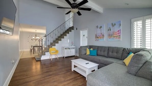 A spacious living room with a grey sofa, a white coffee table, and a staircase leading to an upper floor. - Desert Lily - 6 Pools, Pickle Ball & Tennis Courts, 2 Patios (Palm Springs)