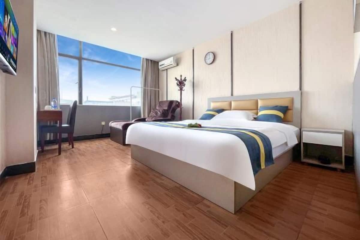 A hotel room with a large bed, a desk, a chair, a TV, and a window with a view.