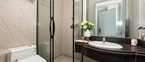 Un baño moderno con cabina de ducha de vidrio, inodoro blanco y encimera de mármol oscuro con lavabo y espejo.
